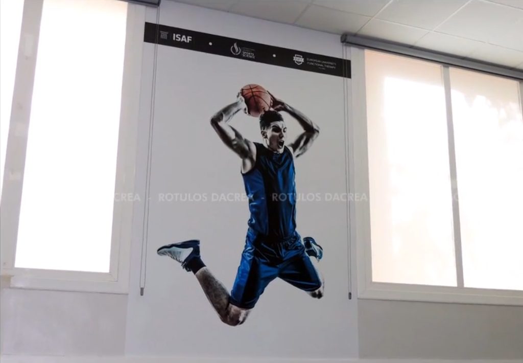 Mural de un jugador de baloncesto impreso sobre la pared entre ventanas del Instituto ISAF