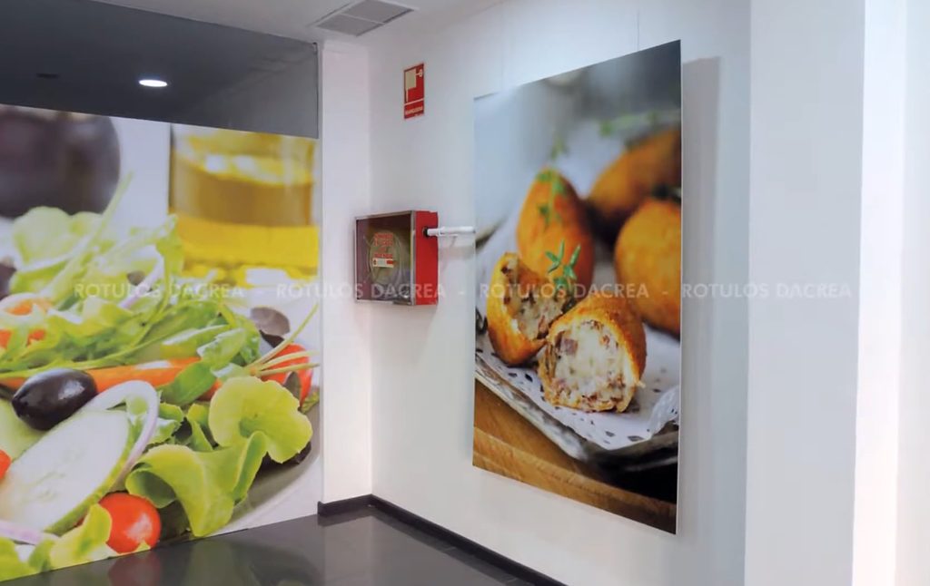 Panel impreso con una fotografía de croquetas sobre la pared del pasillo interior de Casaní